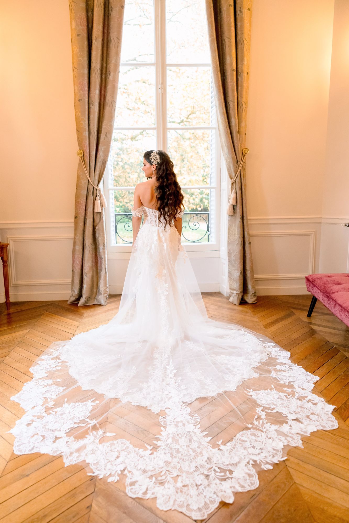 Mariée de dos, robe à traîne devant une fenêtre